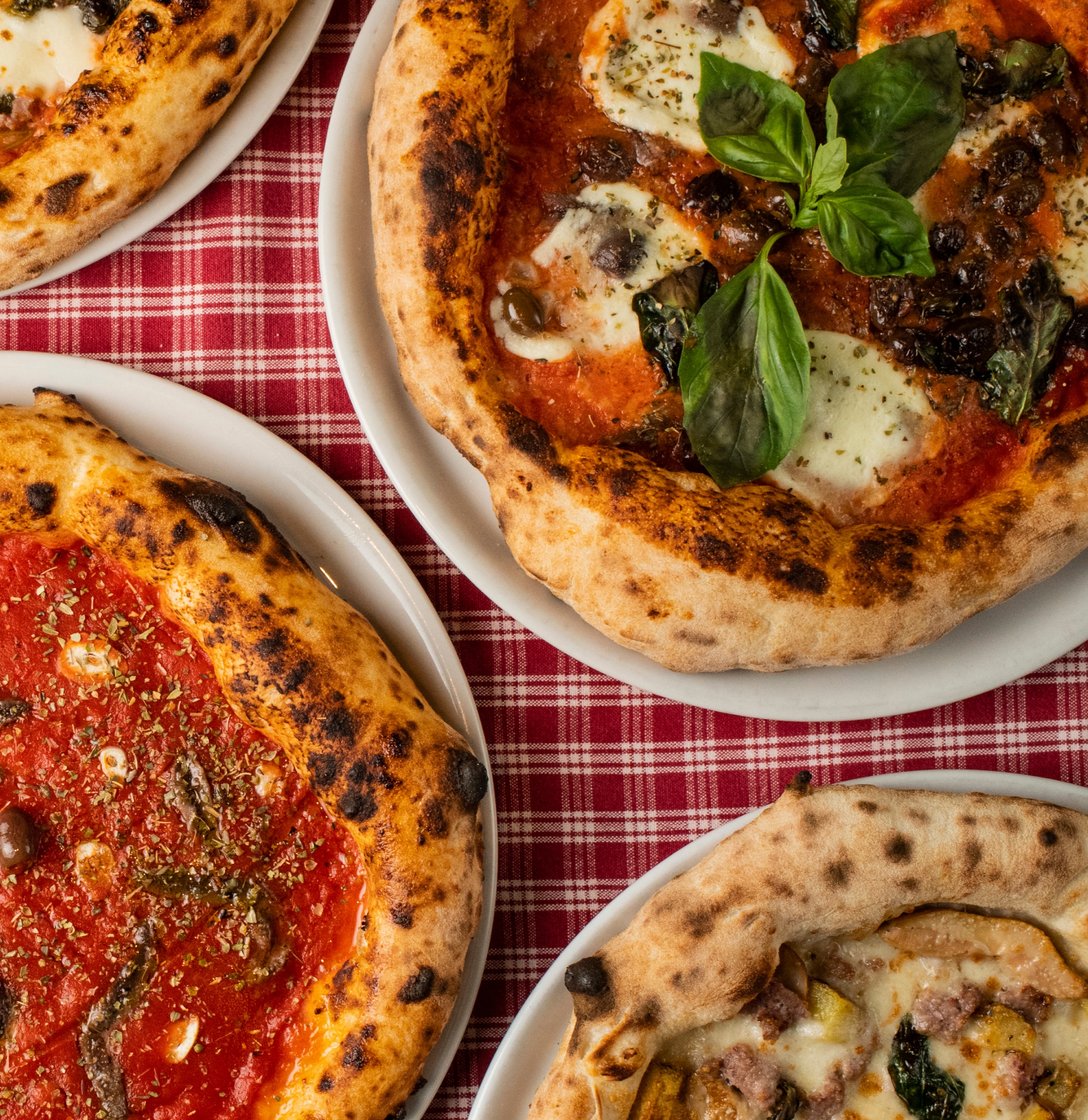 Neapolské pizzy na stole s červeným kostkovaným ubrusem